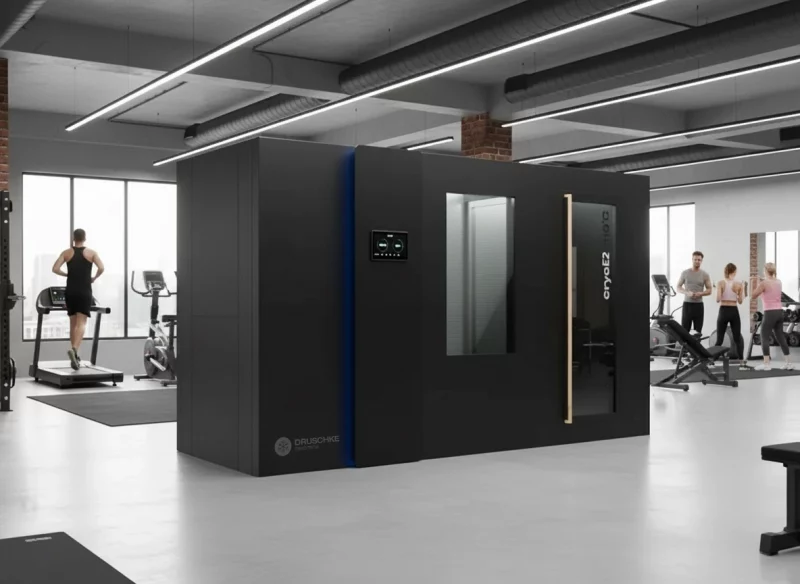 Druschke cryoE2 all-in-one Kältekammer steht in der Mitte eines Fitnessstudios - im Hintergrund trainieren Personen